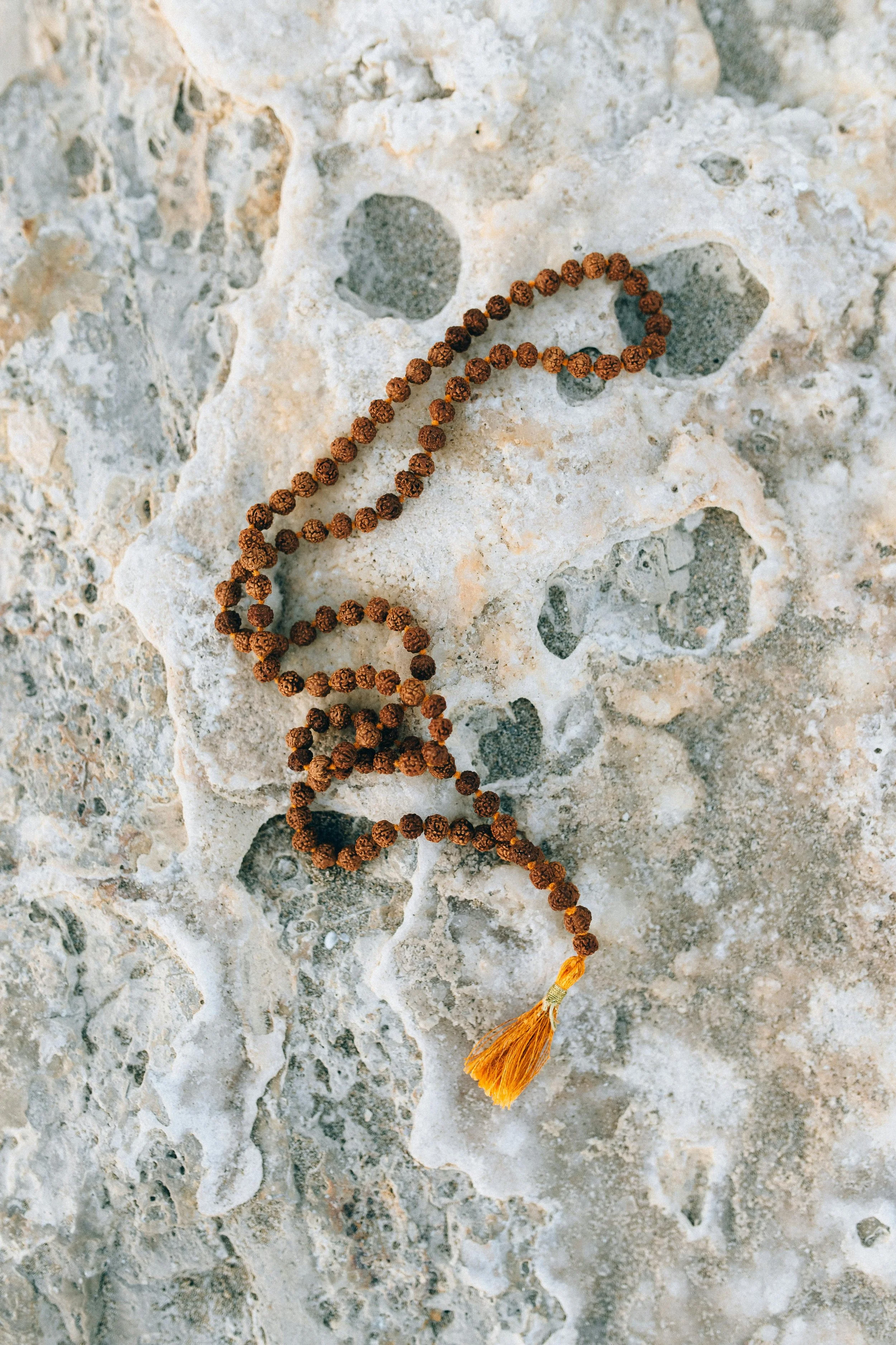 A string of brown prayer beads with a yellow tassel, resting on a textured stone surface.