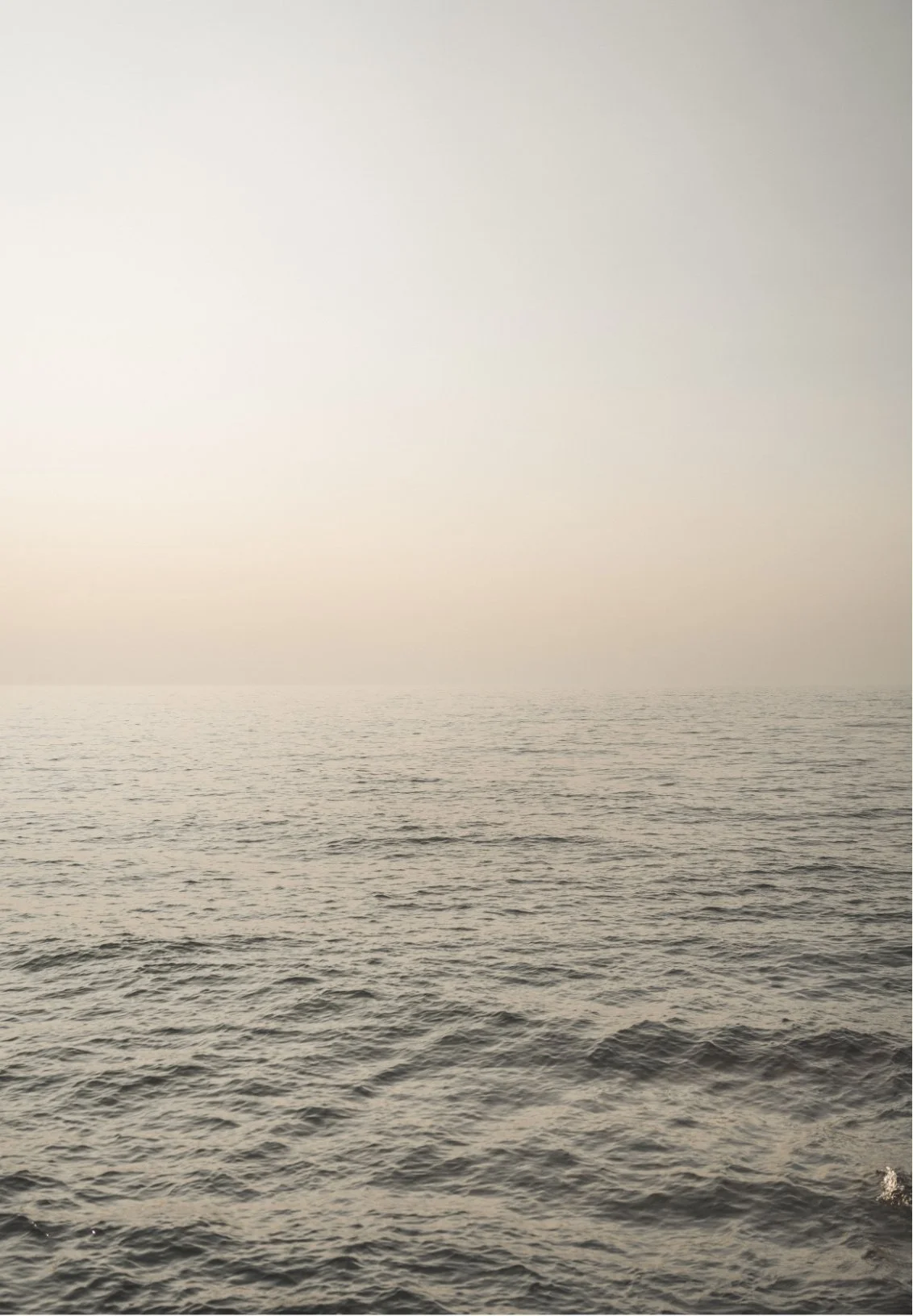 Calm ocean with gentle waves under a foggy sky.