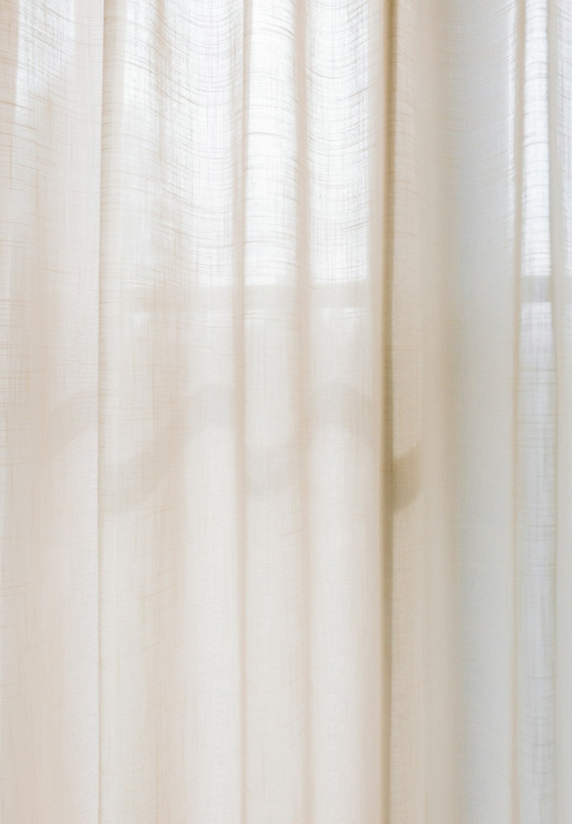 Close-up of cream-colored curtains hanging in front of a window.