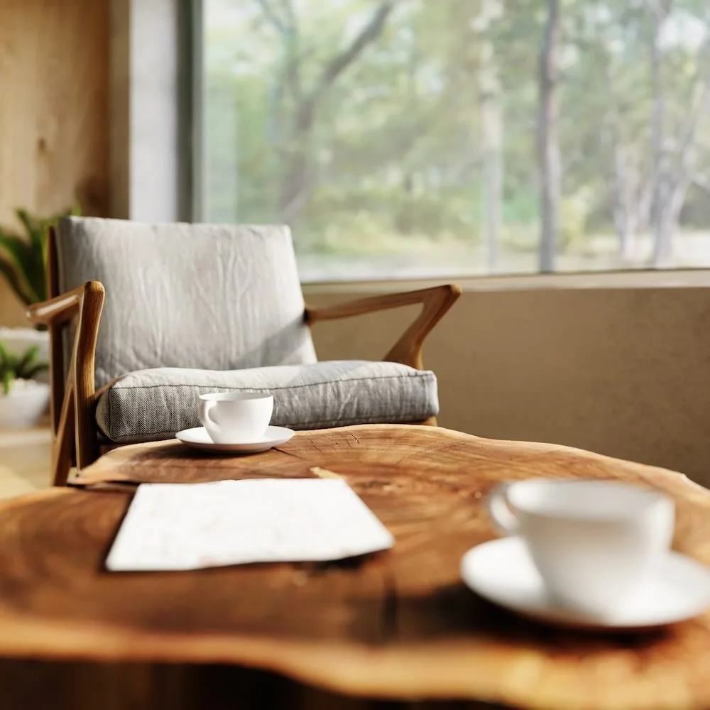 Empty white coffee cups on a wooden table in a cozy room with a sofa and a large window showing trees, representing a welcoming space to get started with emdr therapy.