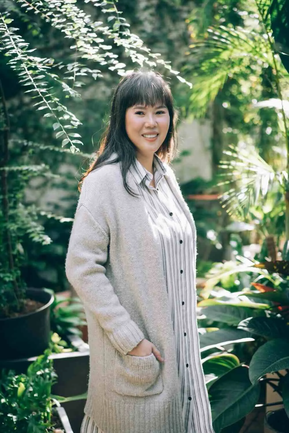 FuFan Chiang, LMFT, a bilingual English and Mandarin EMDR therapist, smiling warmly in a bright, natural outdoor setting with lush green foliage.