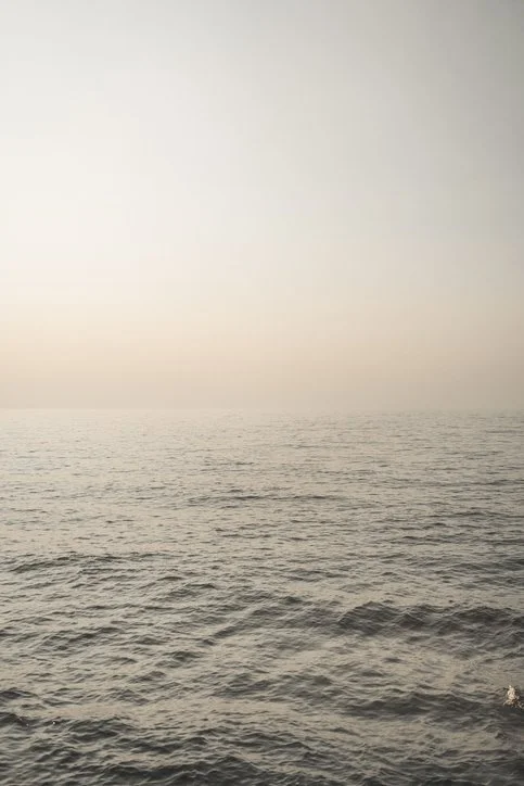 Calm ocean with gentle waves under a hazy sky.