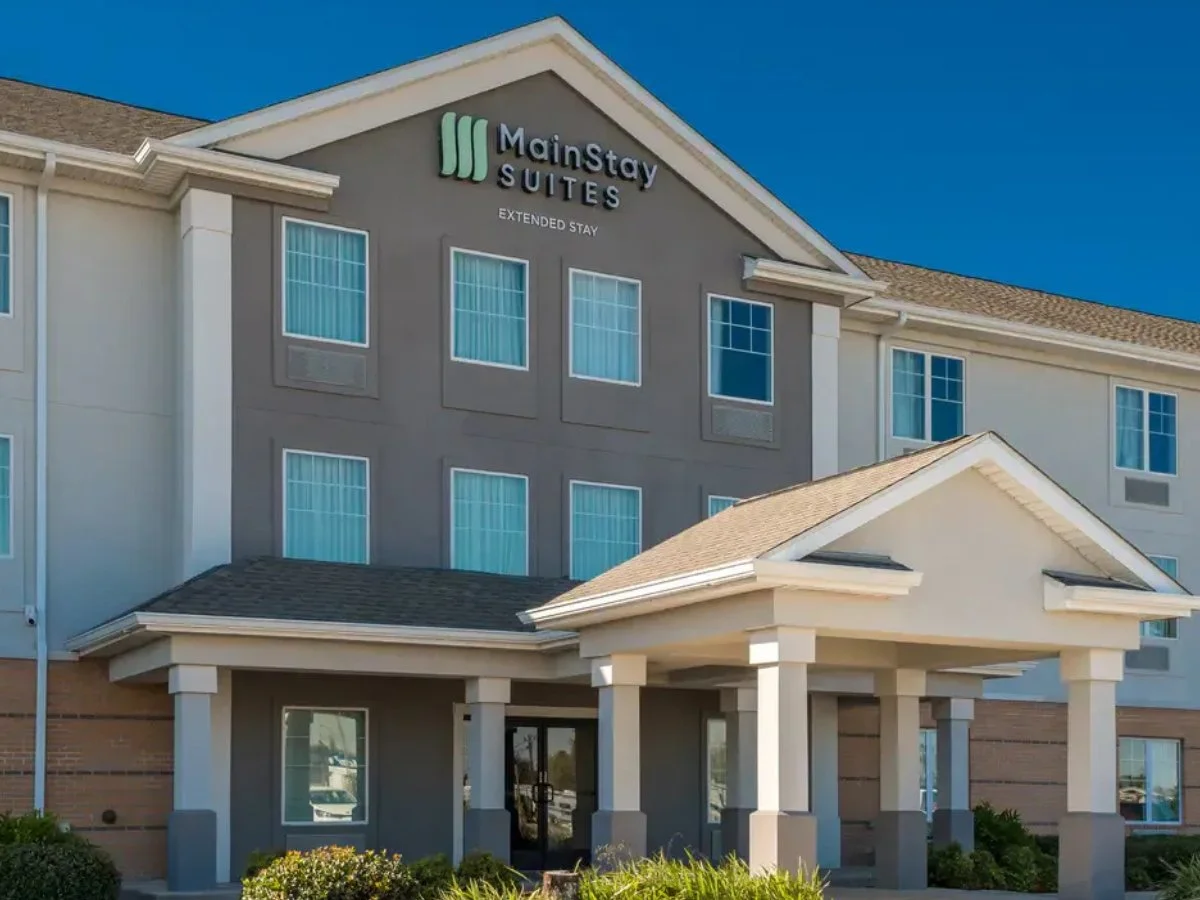 Exterior view of Mainstay Suites hotel building with a covered entrance, multiple floors, and blue sky.