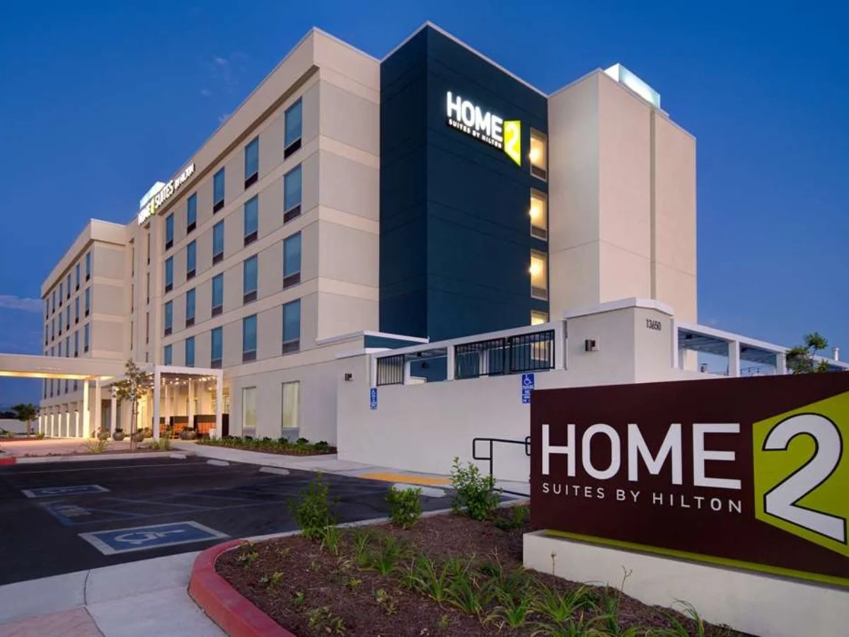 Exterior of a Hilton Home2 Suites hotel building at dusk with a parking lot and signage.