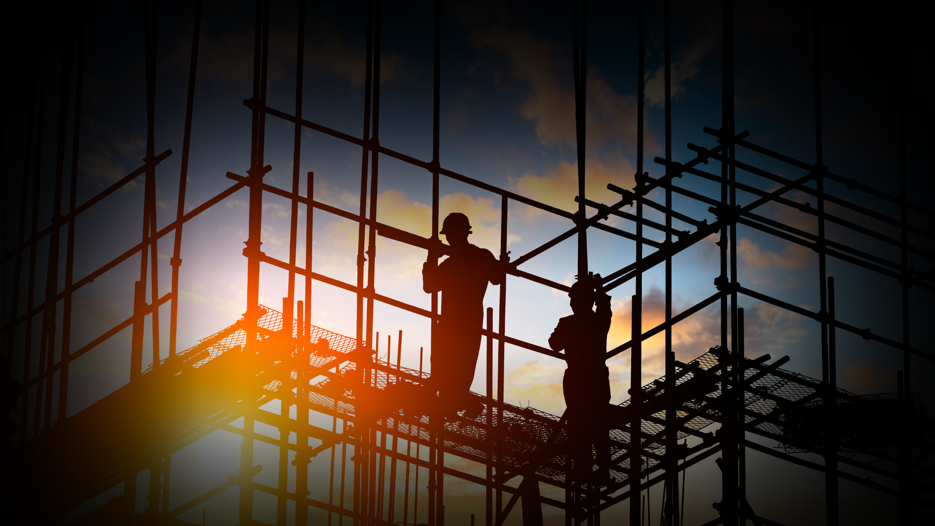 Silhouettes of construction workers on scaffolding during sunset, with a colorful sky in the background.