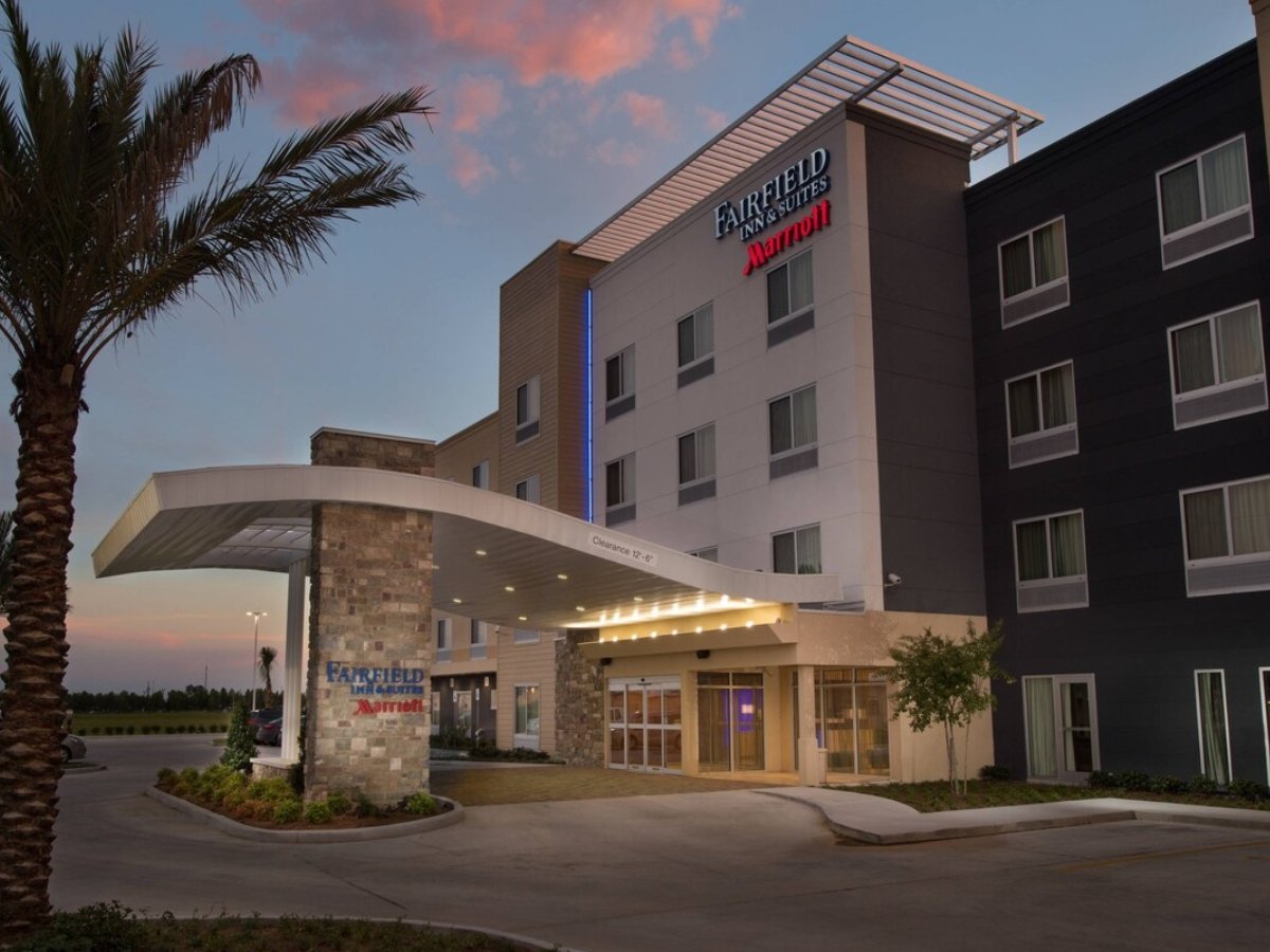 The exterior of a Fairfield Inn & Suites by Marriott hotel during dusk, with a covered entrance, palm trees, and a multi-story building with hotel signage.