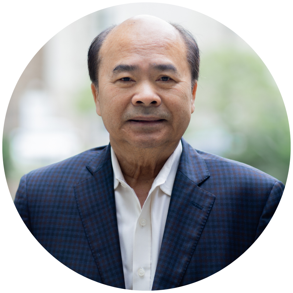 Portrait of a middle-aged Asian man with a receding hairline, wearing a blue checked blazer and white shirt, outdoors with a blurred background.