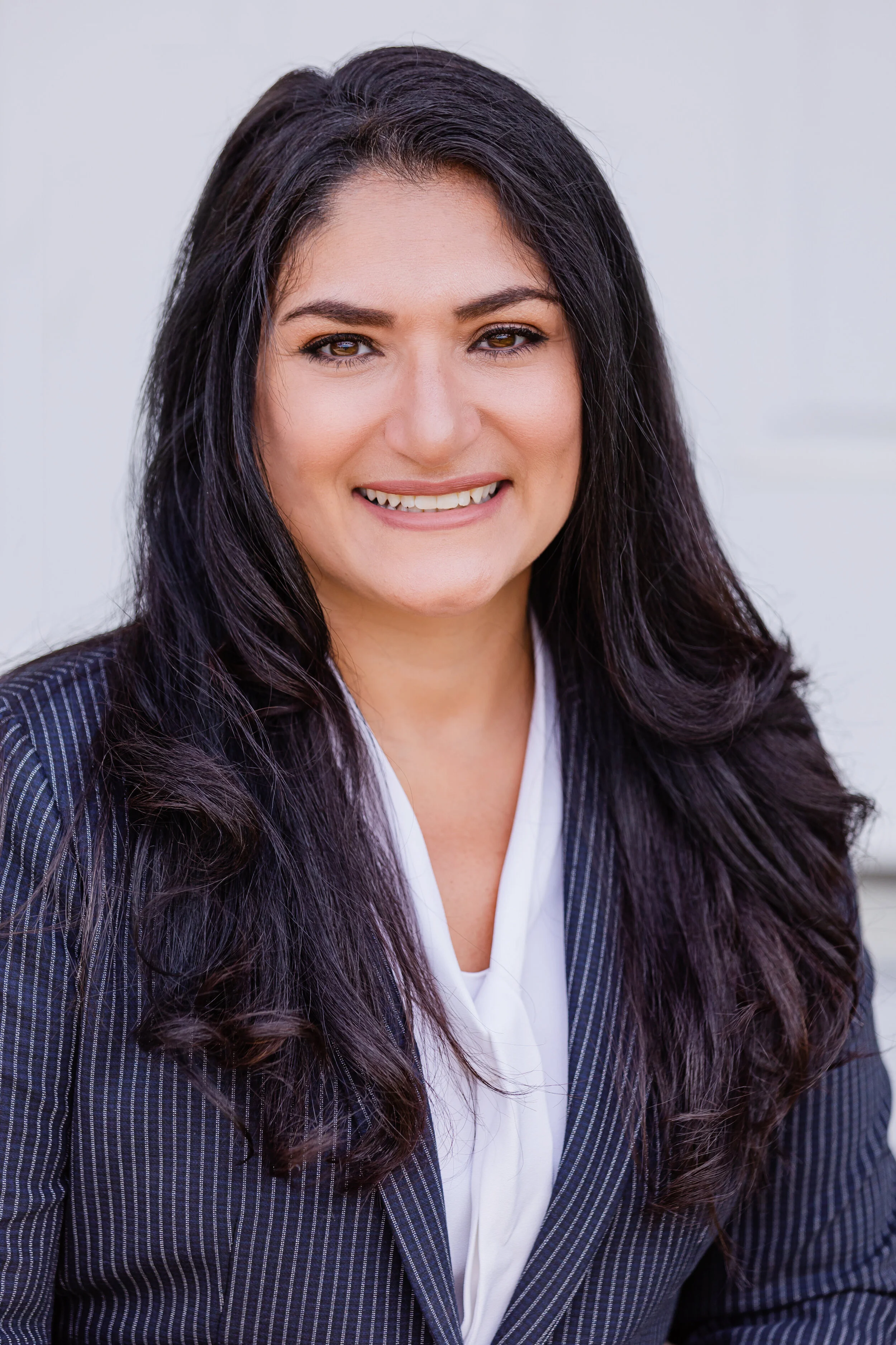 Smiling person with long dark hair in a pinstripe blazer and white shirt