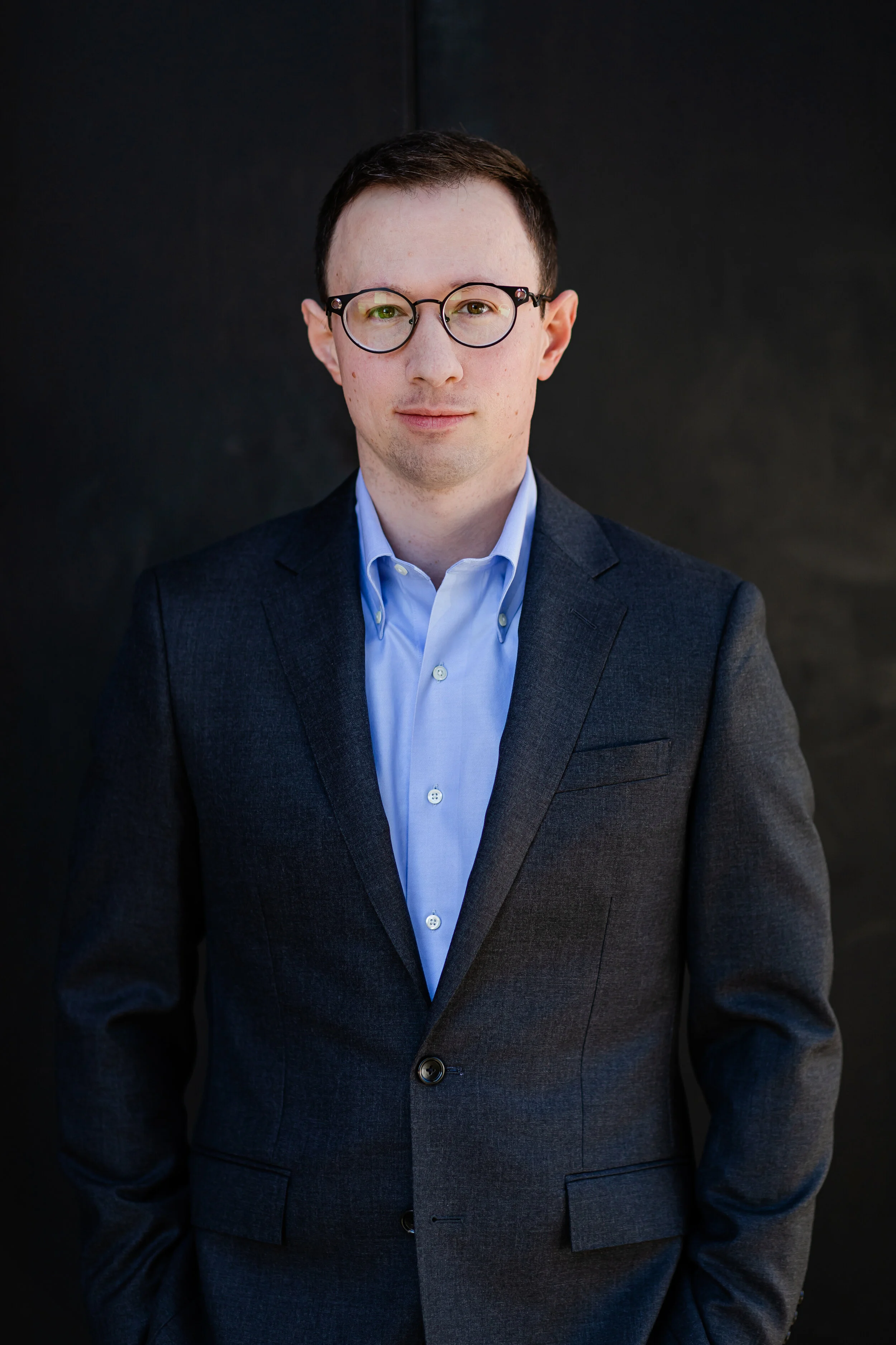 Man in a suit with glasses against a dark background.