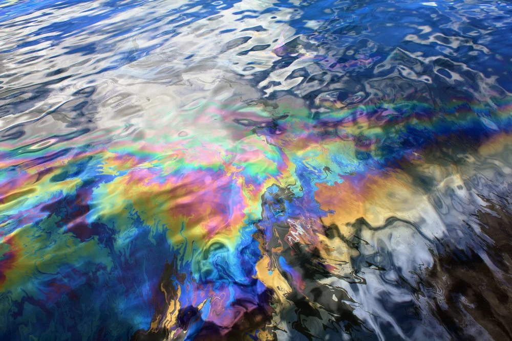 Oil glistens in body of water.
