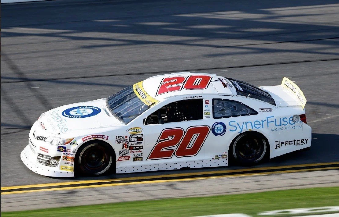 A white race car with the number 20 on it, racing on a track, with sponsor logos including SynerFuse and Factory.