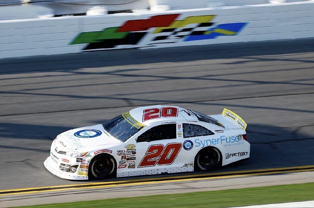White race car with red number 20 and various sponsor logos racing on a track.