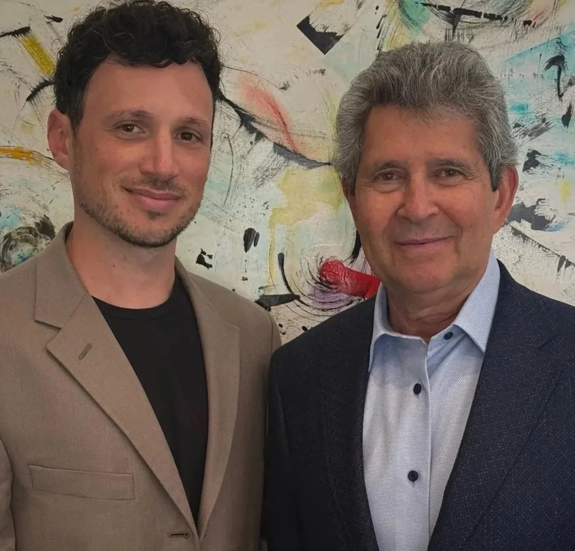 Josh Maya and Isaac Maya from Maya Studios Entertainment. Screenwriters, Producers, Directors. Two men standing in front of an abstract colorful painting, smiling at the camera.