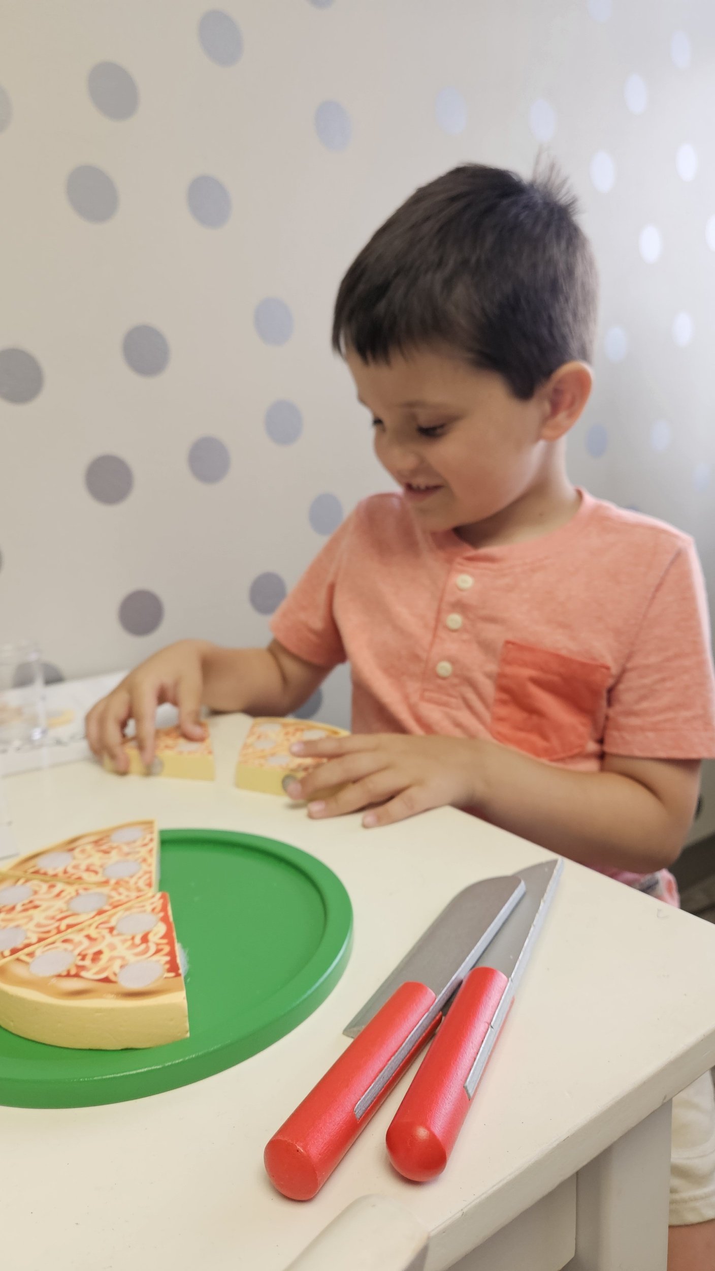 A boy is sitting at the table with a pretend pizza set