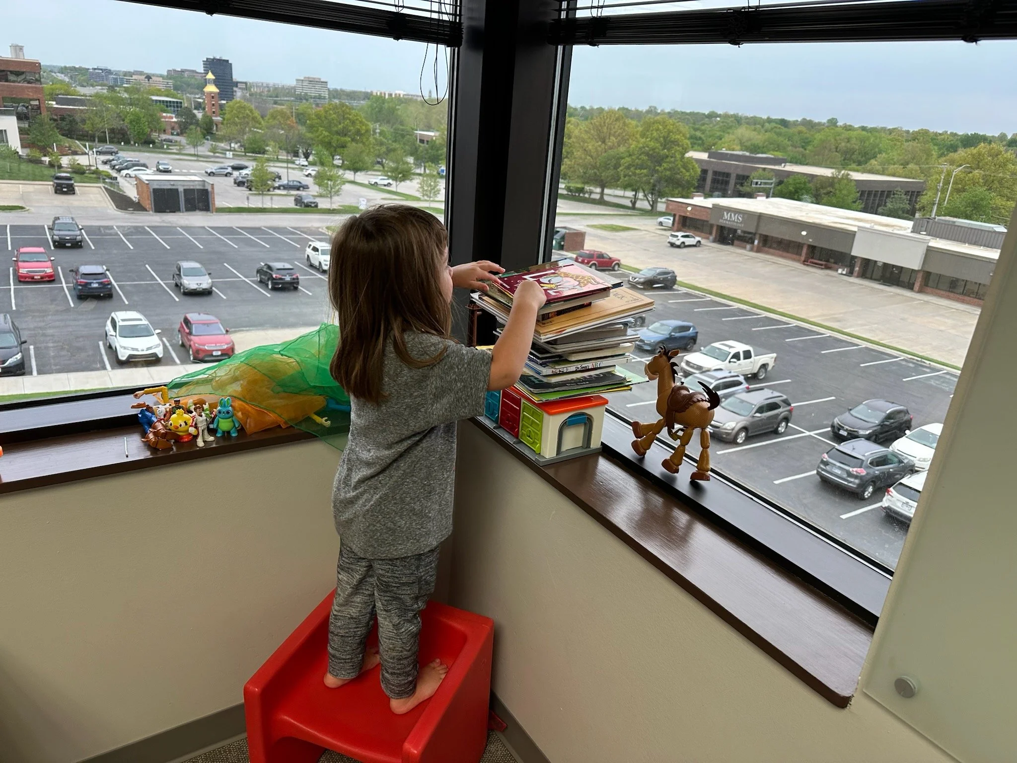 A child is standing at the window playing with toys.