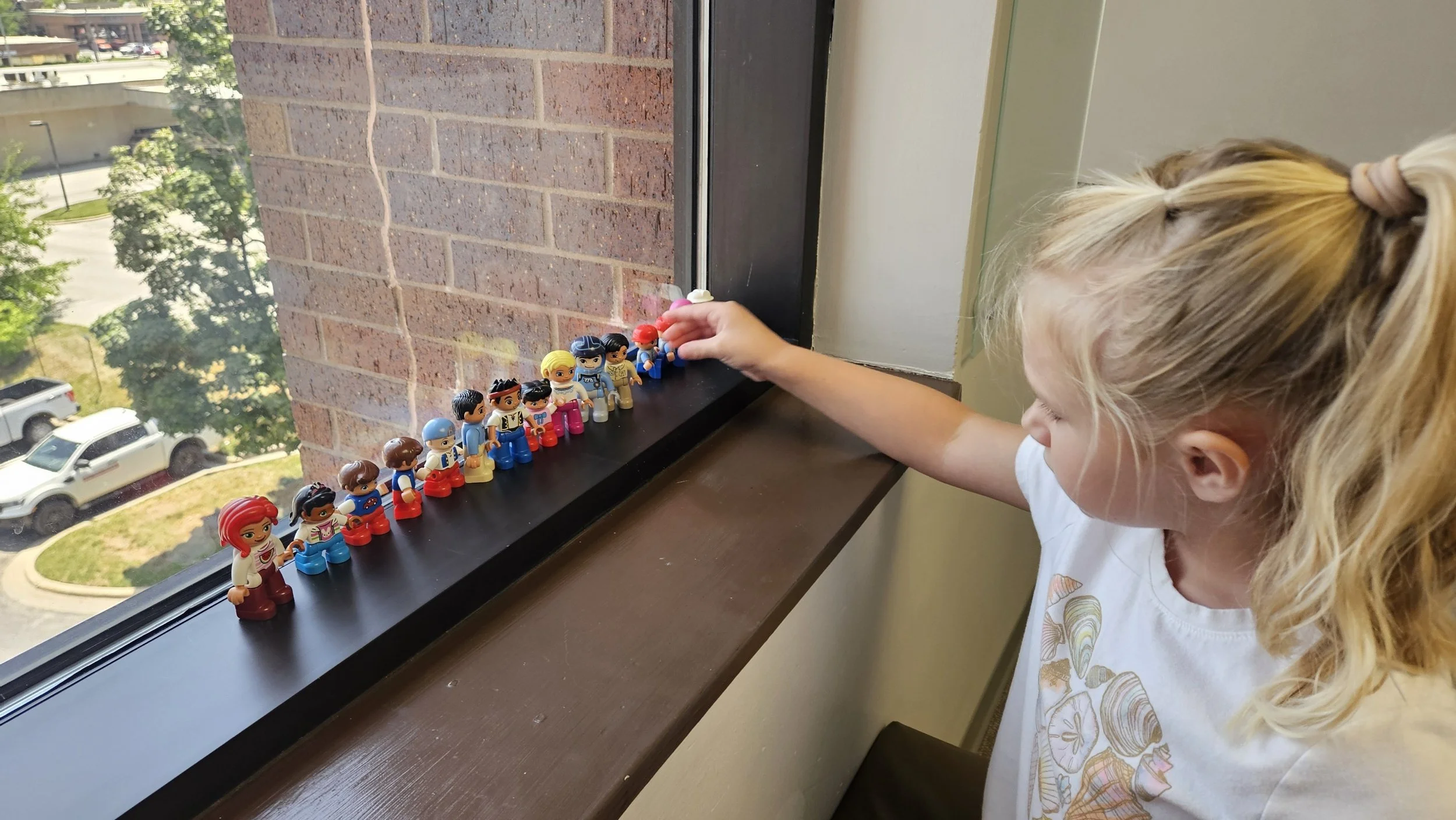 A little girl is organizing a beautiful line of Little People characters in the window