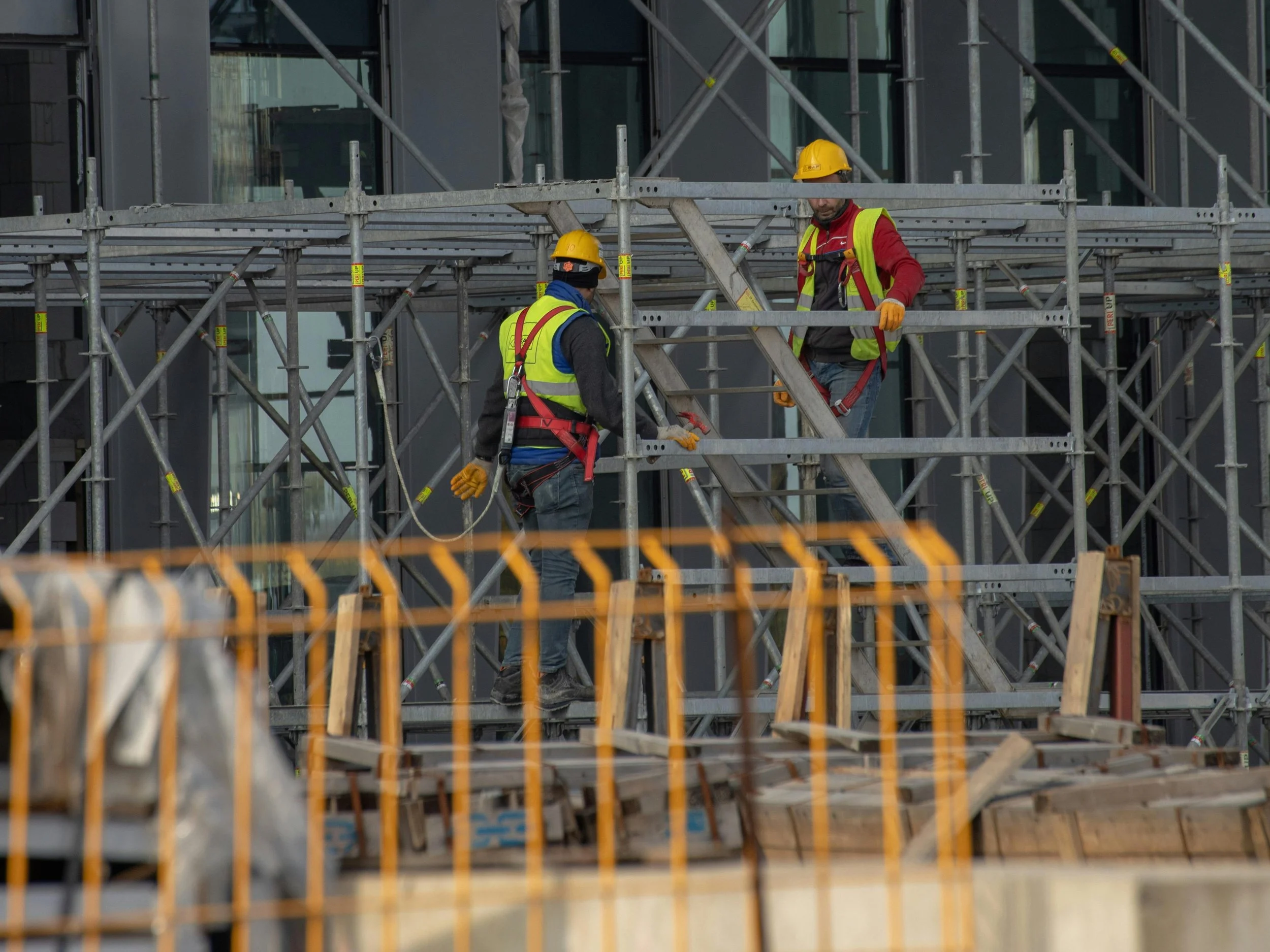 Two construction workers wearing safety helmets and vests working on scaffolding outside a building