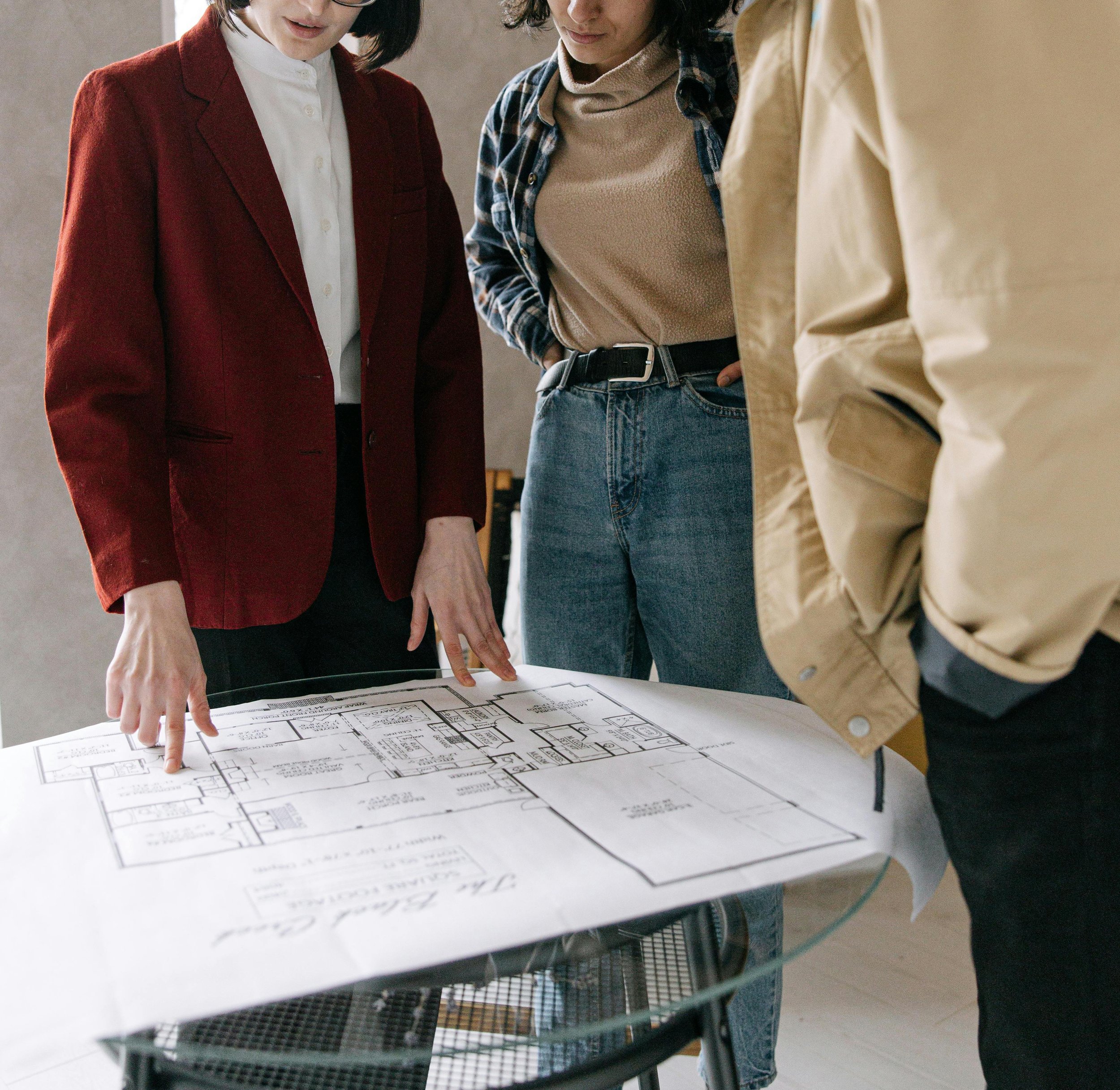 Three people examining a detailed architecture blueprint on a table