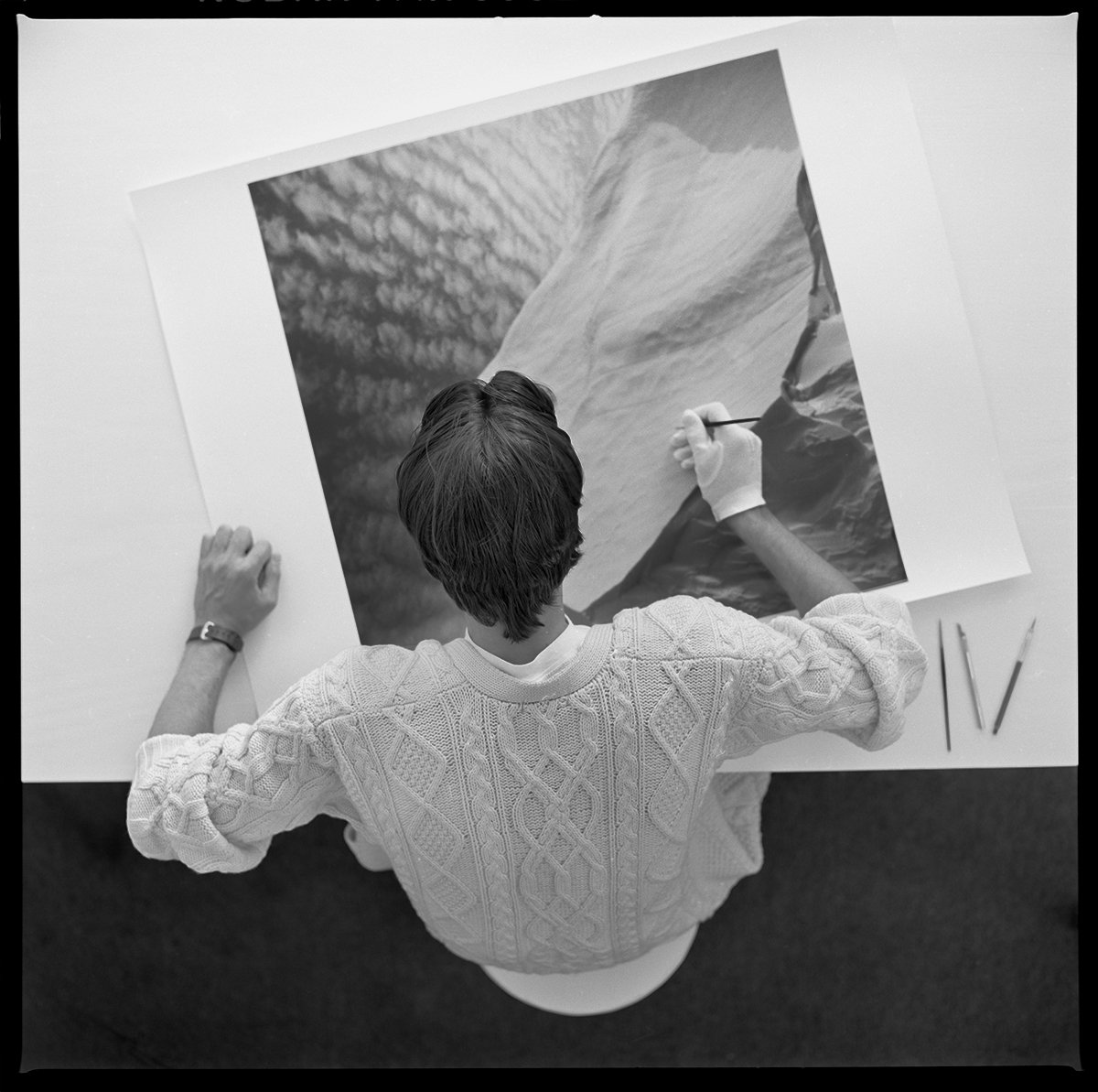 Artist touching up a large black and white landscape photograph on a wall.