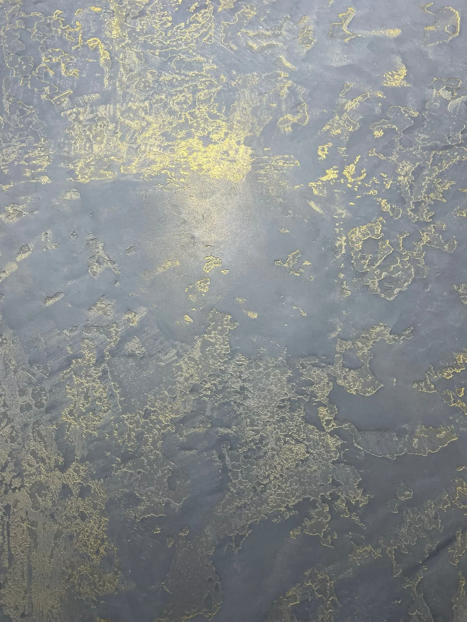 Close-up of a gray surface with gold-colored cracked and peeling paint patterns.