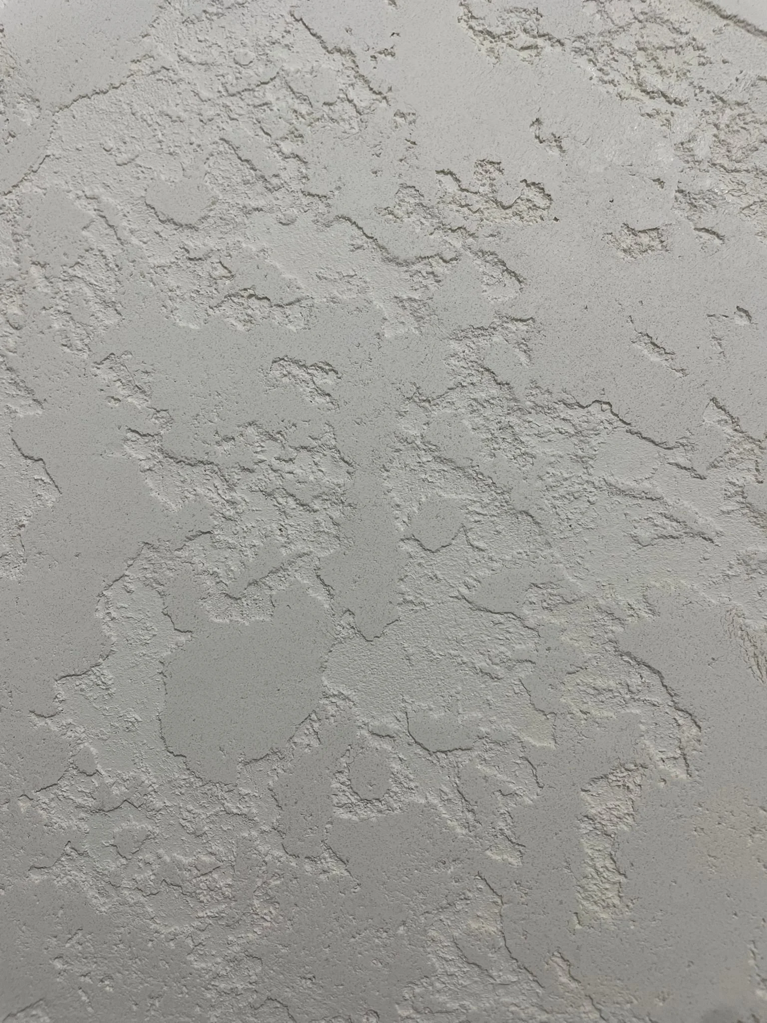 Close-up of a textured white stucco ceiling with rough, uneven surface and visible cracks.