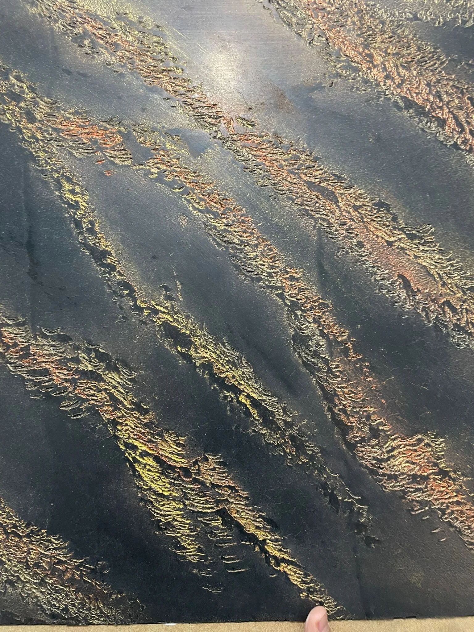 Close-up of a dark, textured surface with iridescent, rust-colored streaks and patches.