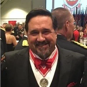 A man in formal attire smiling at an indoor event, wearing a medal around his neck.