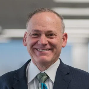 A smiling man in a suit and tie, in an indoor setting.