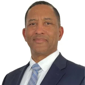 A professional man in a suit with a light blue tie, posing against a white background.