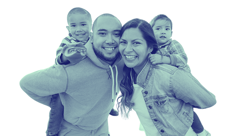 Family of four, including two young children, smiling and posing together. The father and mother are in the center, with the children on their back and shoulders.