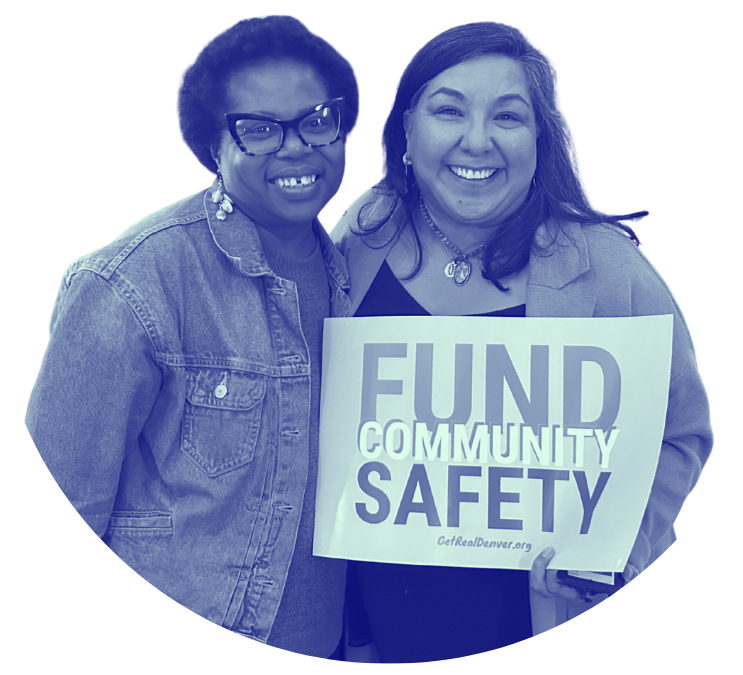 Two women smiling, one holding a sign that says "FUND COMMUNITY SAFETY".
