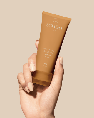 Hand holding a tan tube of Zhou Life scalp and hair sunscreen with SPF 40.