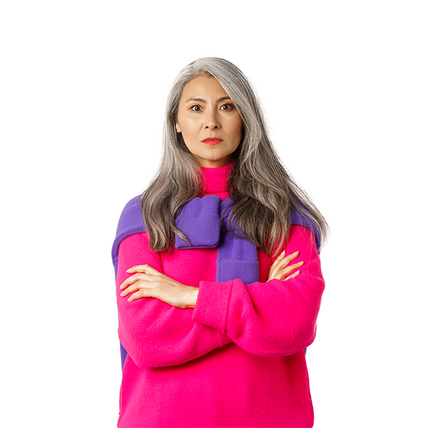 A woman with gray hair wearing a bright pink sweater and a purple and pink scarf, with arms crossed, looking serious.