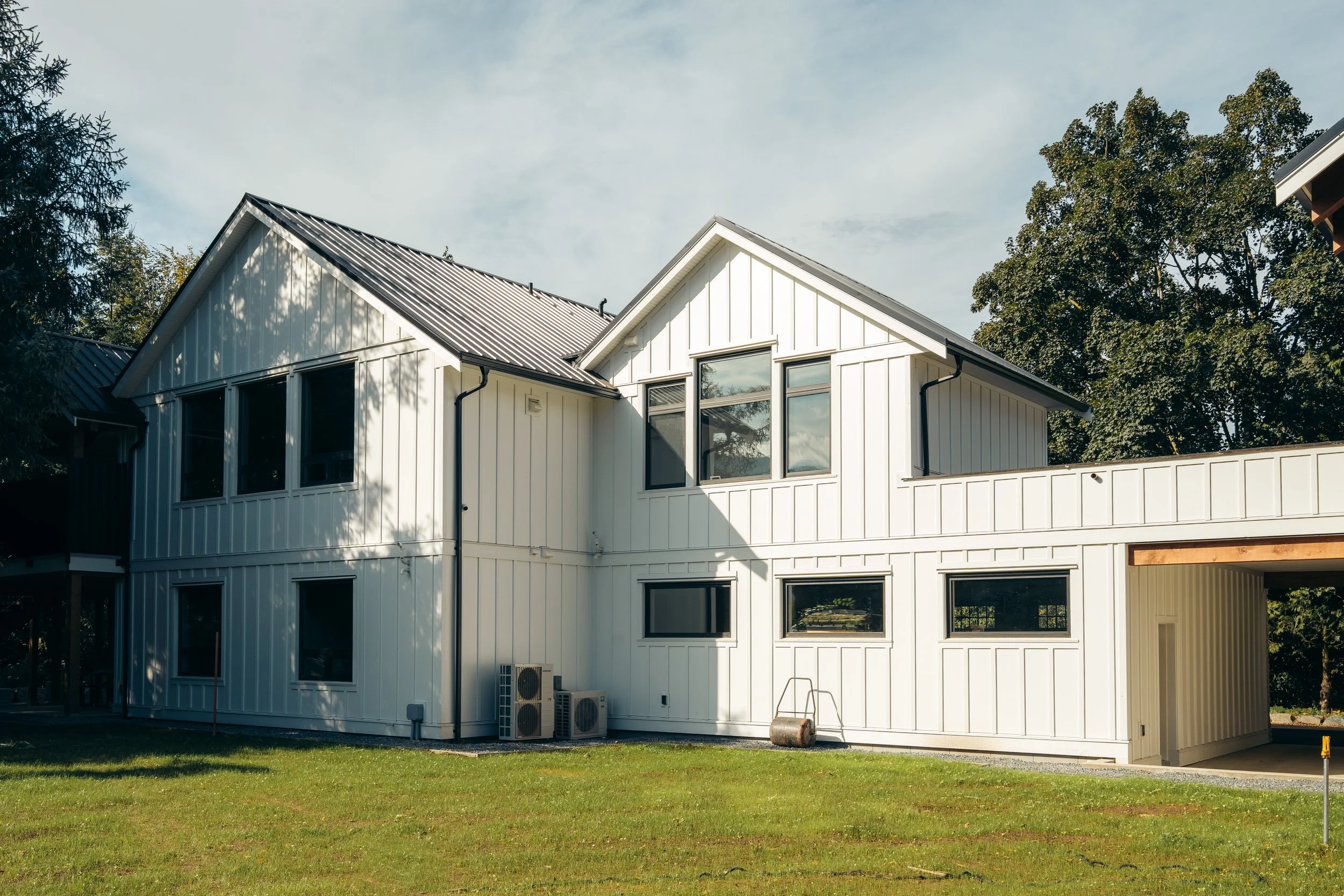 Modern two-story white house with metal roof, multiple windows, and surrounded by green lawn and trees.