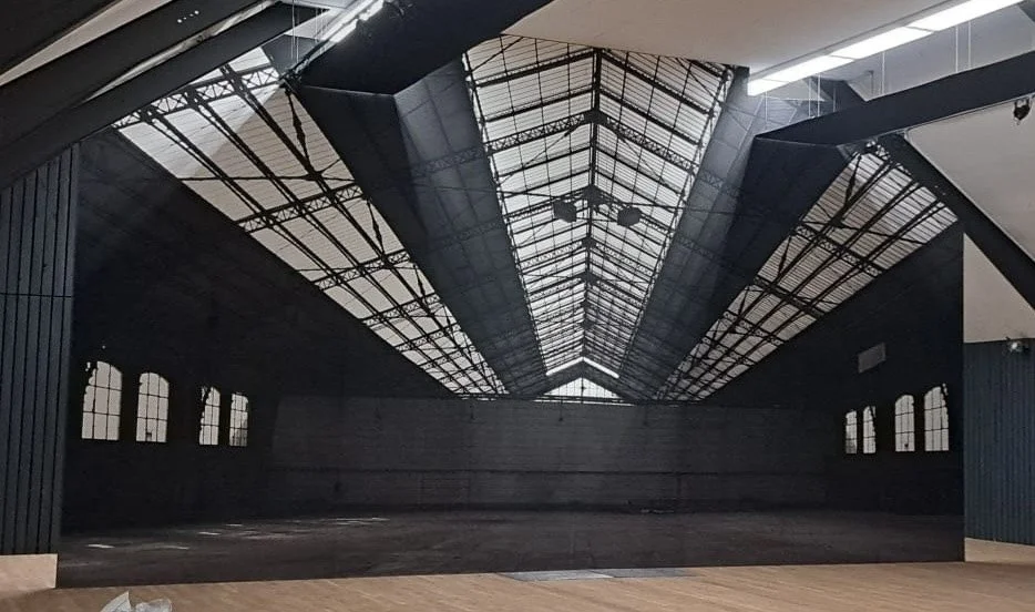 Leeres Industriegebäude mit einer hohen, mit Glas bedeckten Dachkonstruktion und großen Fenstern an den Seiten.