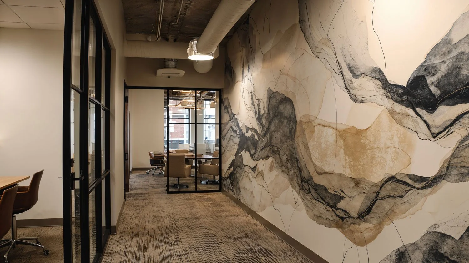 Innenansicht eines modernen Büros mit einer großen Wand, die künstlerisch gestaltet ist, und einem Durchgang, der zu einem Besprechungsraum mit Tischen und Stühlen führt.