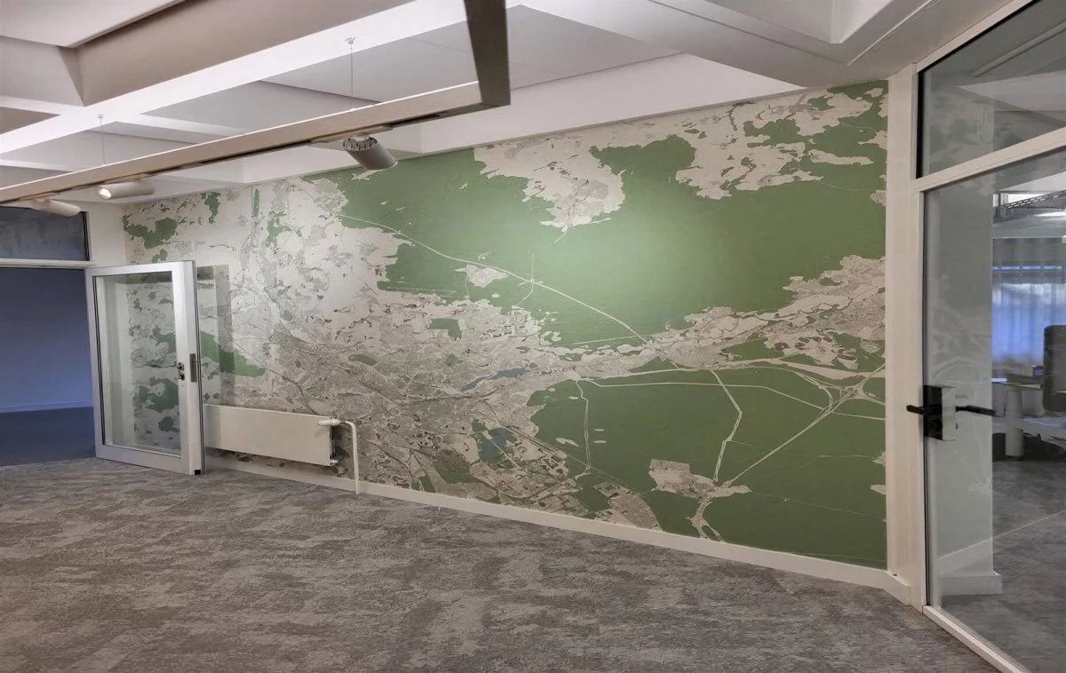Wand mit einer großen Karte oder Karte-ähnlichem Wandbild in einem Büro oder Raum, teils grün, teils grau.