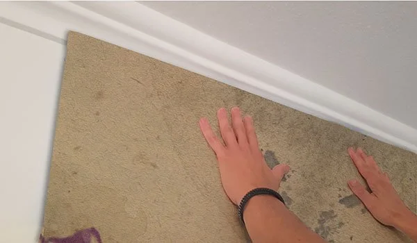 6. Erste Bahn ansetzen und ausrichten.

Die Bahn oben an der Wand anlegen und am Lot ausrichten.
Mit der 5 cm Zugabe können leichte Wandtoleranzen ausgeglichen werden.
Die Bahn von oben nach unten in das Klebebett einlegen und blasenfrei andrücken.
K