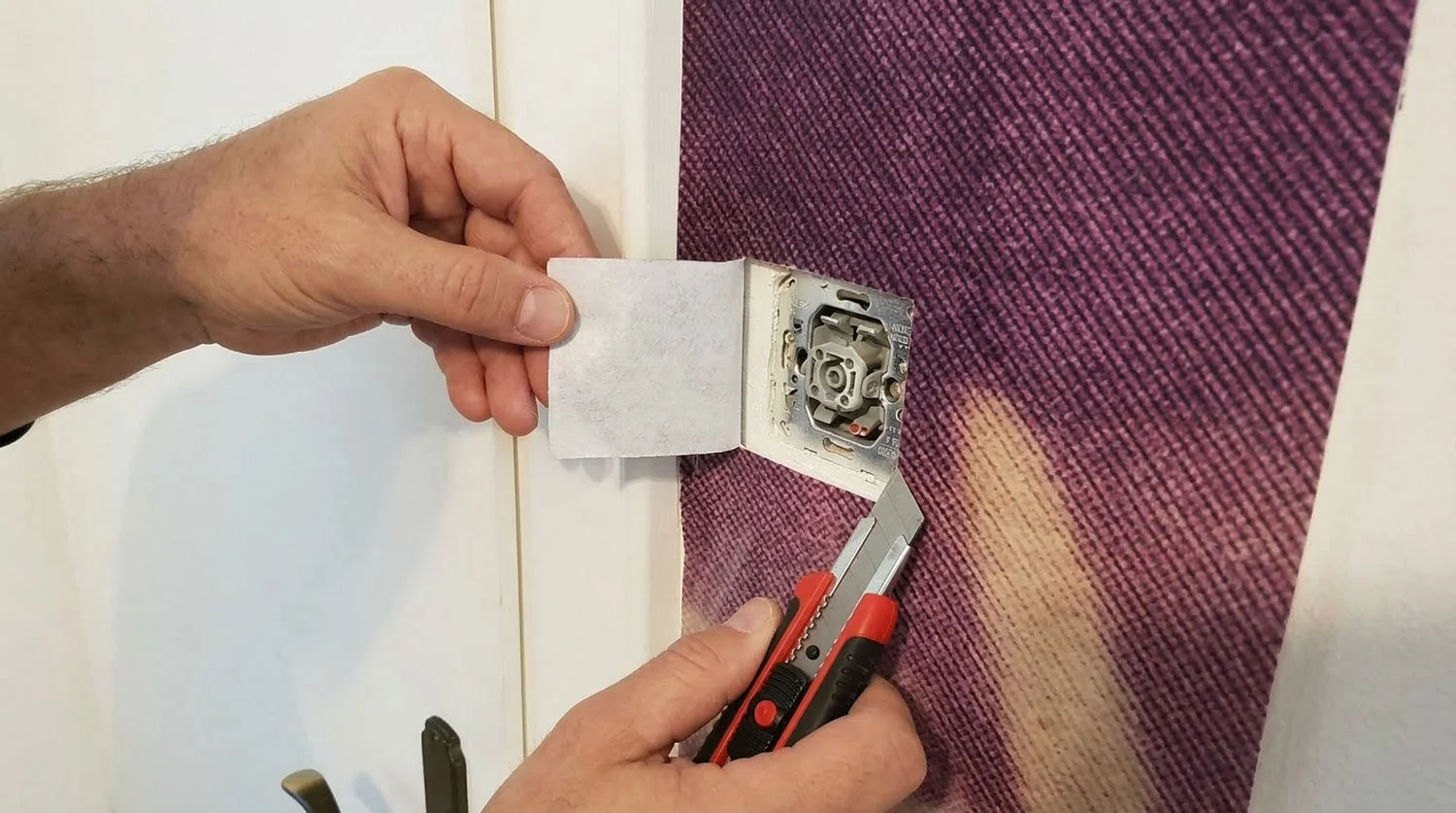 Hand, die einen Elektronik-Schalter in einer Dose in einer Wand installiert, mit einem Messer.