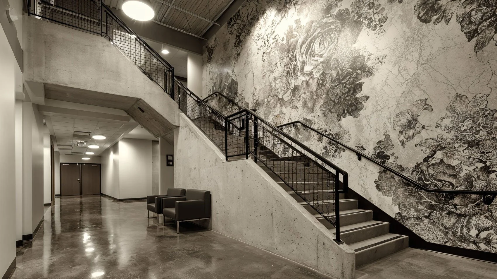 Innenansicht eines Gebäudes mit einer Treppe, einer Wand mit Blumenmuster und Sitzgelegenheiten.