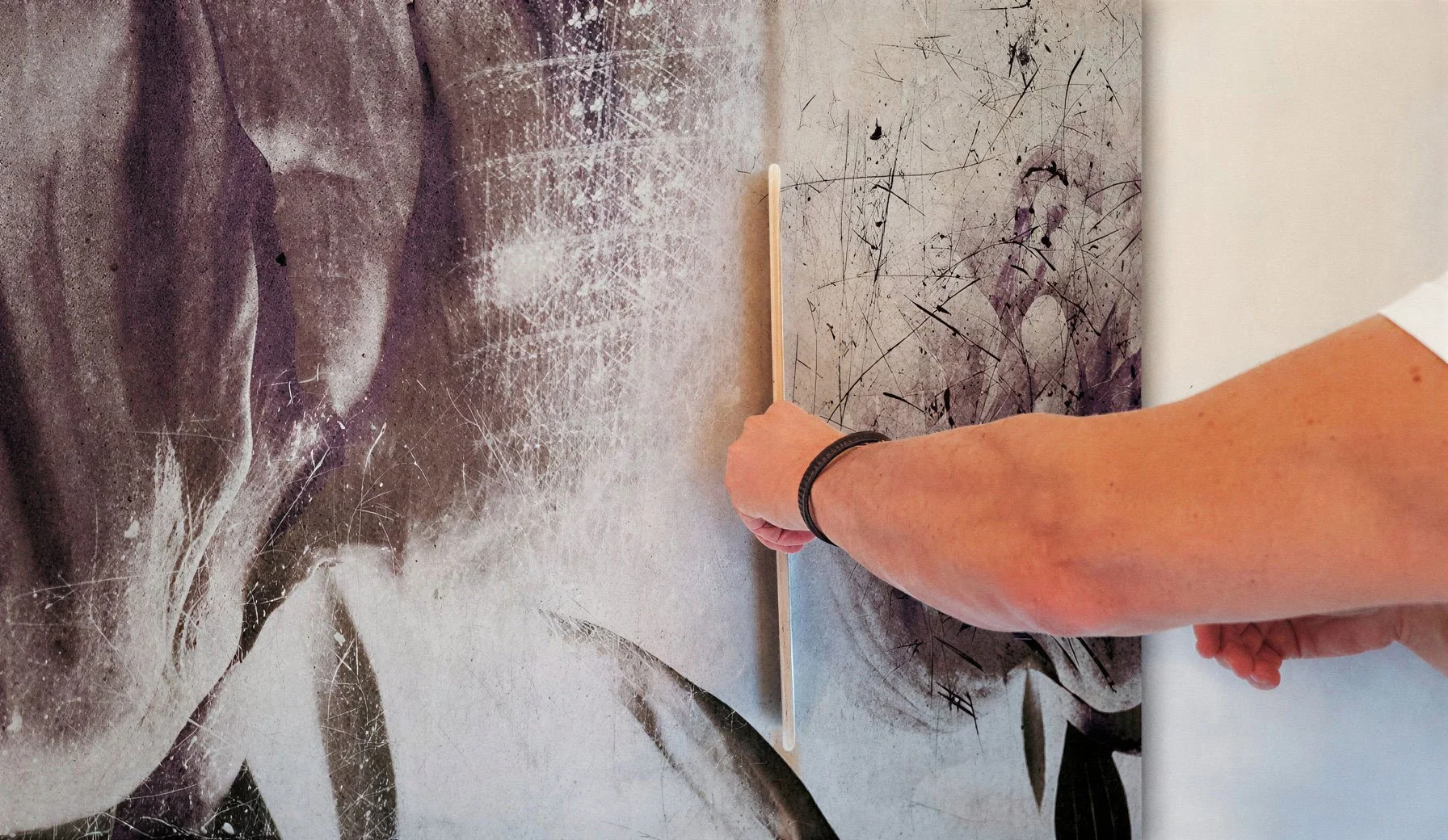 Ein Arm hält einen Pinsel vor einer abstrakten Kunstinstallation mit gesprühten und gestrichelten Mustern auf einer Wand