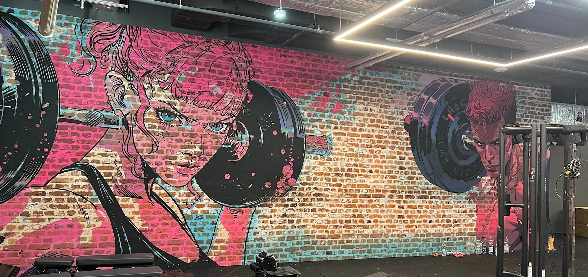 Graffiti-Kunst im Fitnessstudio mit einer Frau und einem Mann, die Gewichte heben, in einer urbanen, industriellen Umgebung.