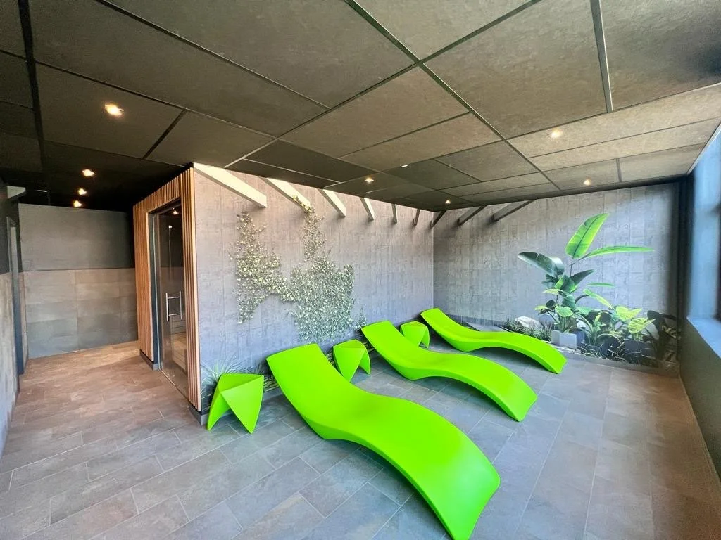 Moderne Sauna mit schwarzen Wänden, grünen Liegen, Pflanzen und einer Wand mit einer Metallskulptur in Form eines Tieres.