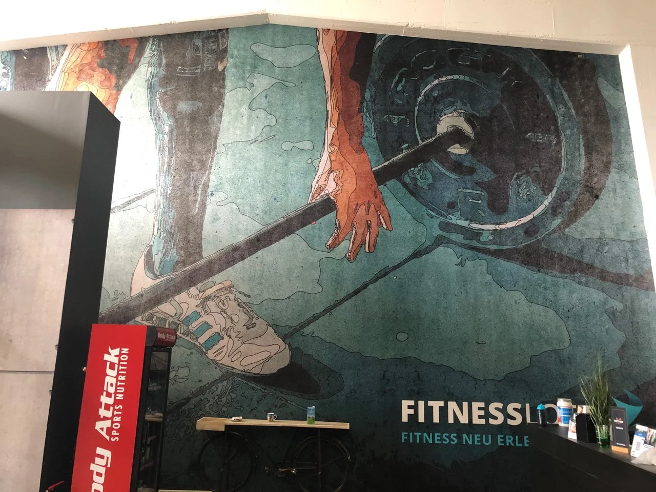 Wandgemälde eines Hand- und Armprojektils auf einer Fitnessstudiowand, darunter das Schriftzug 'FITNESSLOFT' und der Slogan 'FITNESS NEU ERLE'.
