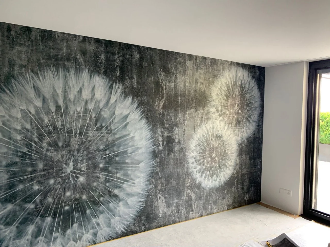 Wand mit Wandbild von weißen Pusteblumen auf dunklem Hintergrund in einem modernen Raum mit großem Fenster