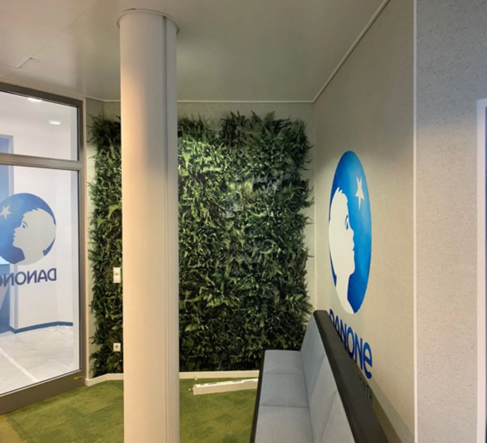 Wartebereich mit Wanddekoration und begrüntem Hintergrund, Sitzbank und Fenster mit Logo.