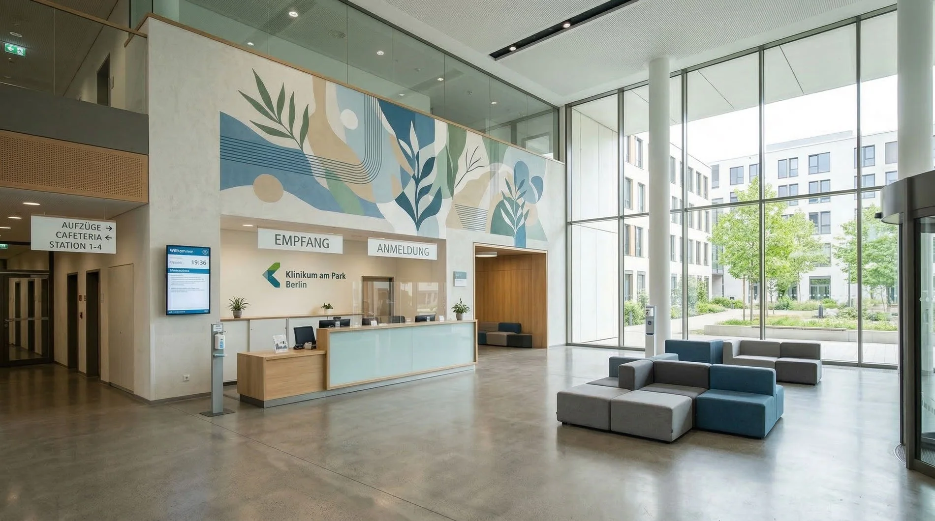 Hospitaleingang mit Empfangstresen, Sitzgelegenheiten und großen Fenstern, die einen Blick auf einen grünen Innenhof mit Bäumen bieten.