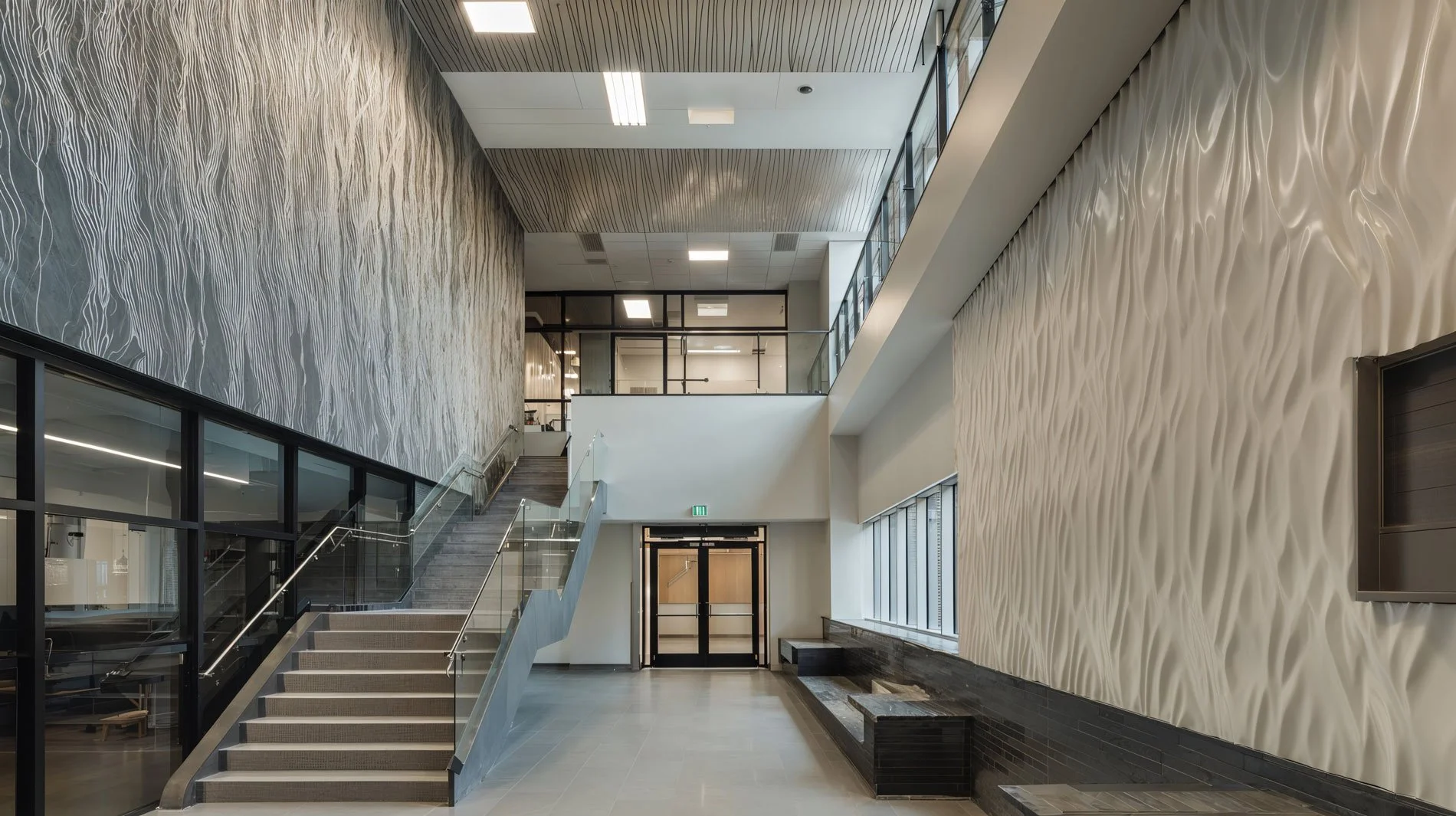 Moderner, heller Eingangsbereich eines Bürogebäudes mit stilvollen Wanddekorationen, Treppe auf der linken Seite, große Fenster auf der rechten Seite, und Sitzbänken an der Wand.