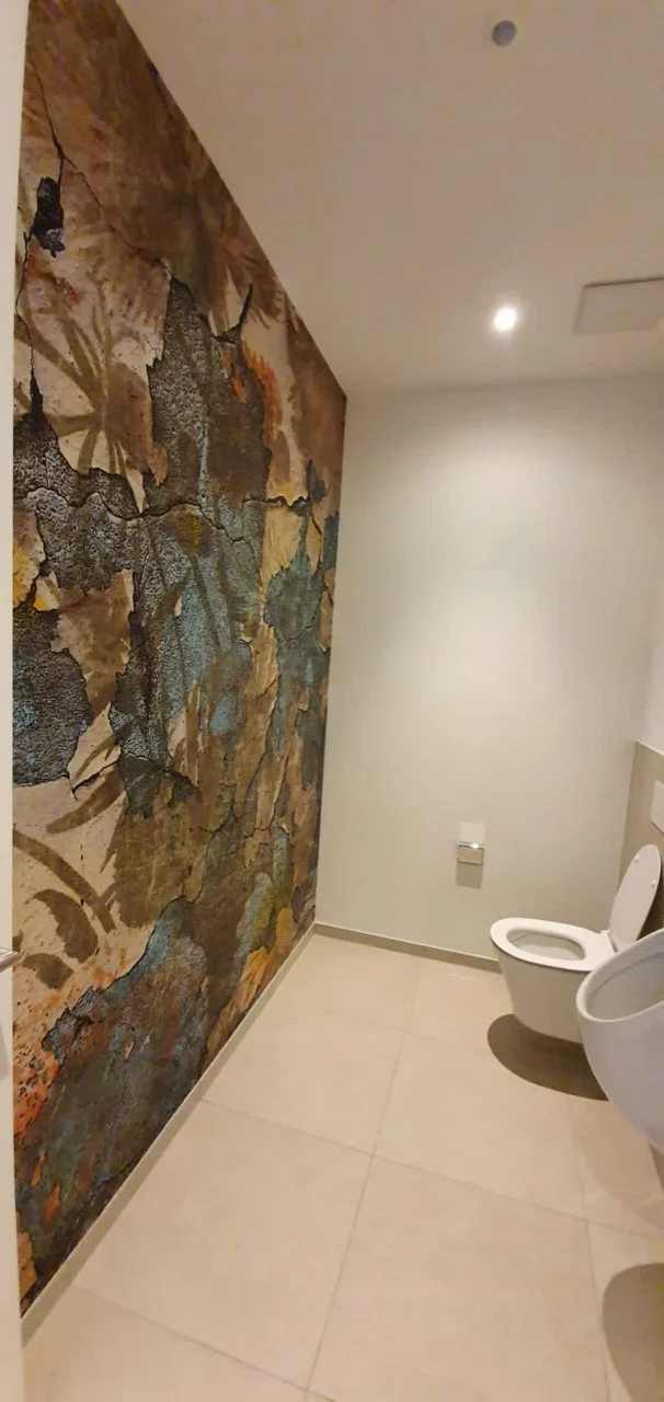 Ein Badezimmer mit einer dekorativen Wandtapete, die Muster von Blättern und Natur zeigt, und einer weißen Toilette.