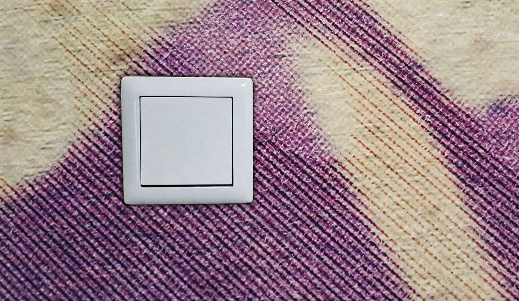 Weißer Lichtschalter auf einem bunten Teppichboden mit gemustertem Design.